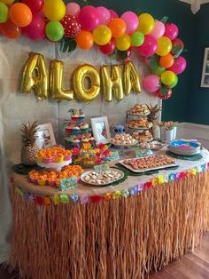 an aloha themed dessert table with balloons and tassels on the wall