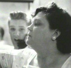 black and white photo of two people sitting next to each other with one woman looking at the camera