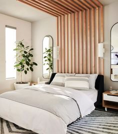 a white bed sitting in a bedroom next to a mirror and potted plant on top of a dresser