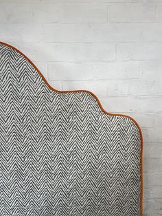 an upholstered headboard made with herringbone fabric and leather piping, against a white brick wall