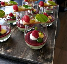 desserts are arranged in small glass dishes on a wooden table with green leaves and raspberries