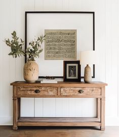 a wooden table with two vases on top of it and a framed photograph above it