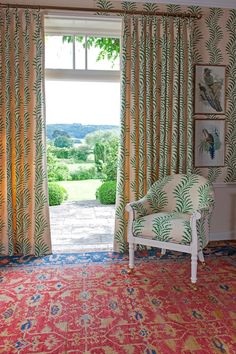 an open window with curtains and a chair in front of it, next to a red rug