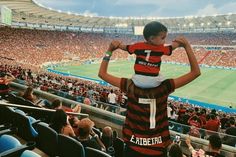 a young boy holding onto his father's shoulders at a soccer game in a stadium