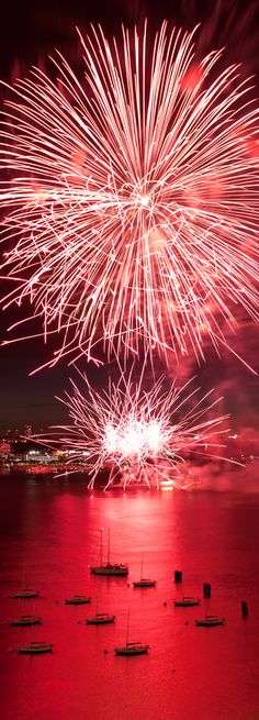 fireworks are lit up in the night sky over boats on the water with red lights