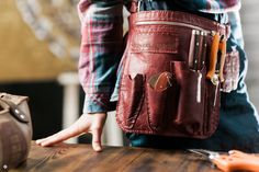 a person holding a leather tool bag on top of a wooden table