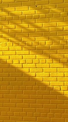 a yellow brick wall with the shadow of a tree casting a long shadow on it