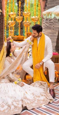 a man kneeling down next to a woman in a white and yellow wedding dress on the ground