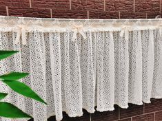 a white curtain hanging on the side of a brick wall next to a green plant