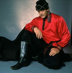 a man in a red shirt and black pants sitting on the ground with his legs crossed