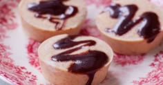 three cupcakes with chocolate icing on a red and white plate