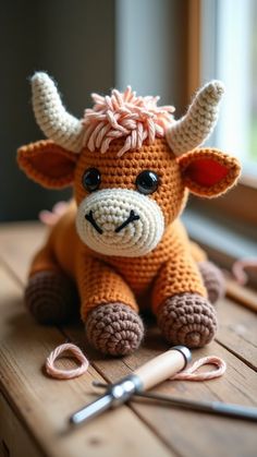 a crocheted cow sitting on top of a wooden table next to a pair of scissors