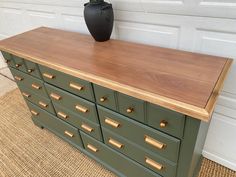 a large green dresser with gold handles and knobs on the top, sitting in front of a white garage door