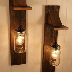 two mason jars are hanging on the wall next to each other with lights in them