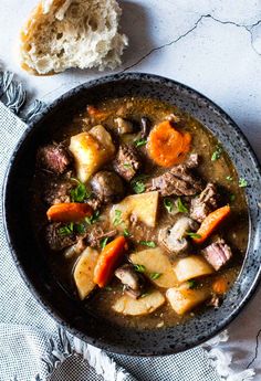 a bowl of stew with meat, potatoes and carrots next to a piece of bread