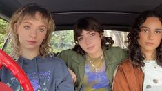 three women are sitting in the back of a car and one is looking at the camera