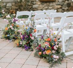 rows of white chairs with colorful flowers on the back are lined up for an outdoor ceremony