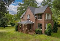 a red brick house in the middle of a green field with trees and bushes around it