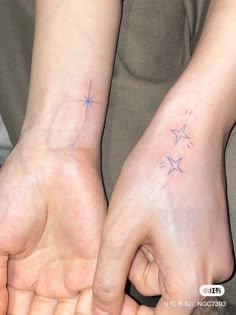 two people holding hands with small stars on their wrist tattooing each other's fingers