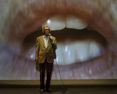 a man standing in front of a large screen with his mouth open while holding a microphone