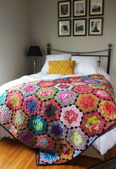 a bed with a colorful quilt on top of it next to two framed pictures and a lamp