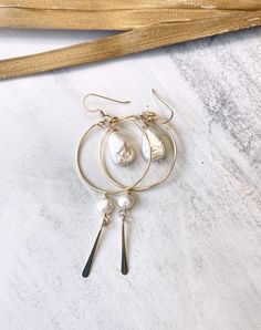 Embrace the carefree beachy boho vibe with these stunning gold hoops. Featuring a fresh water pearl nugget suspended at the center, these earrings are accented with a 1 1/2 inch chain adorned with delicate moonstone gemstones. A unique blend of pearl and moonstone, these earrings are perfect for adding a touch of coastal elegance to any outfit. All materials are gold filled. Approximately 2 1/4 inches in length. Brass Dangle Jewelry With Pearl Charm, Bohemian Dangle Earrings With Pearl Charm, 14k Gold-filled Silver Jewelry With Pearl Charm, Silver 14k Gold-filled Jewelry With Pearl Charm, Gold Bohemian Jewelry With Pearl Charm, Silver Jewelry With Pearl Charm In 14k Gold, Bohemian Pearl Pendant Jewelry, Bohemian Gold Jewelry With Pearl Charm, Adjustable Bohemian Pearl Drop Jewelry