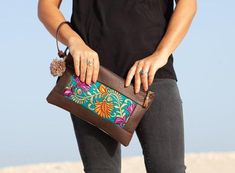 a woman holding a brown purse with colorful designs on the front and side, while wearing black jeans