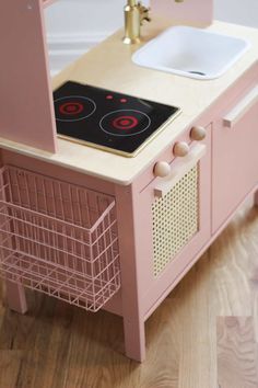 a pink toy kitchen with a stove top and sink in the center, on a wooden floor