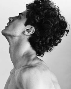 a man with curly hair and no shirt looking up to the sky in black and white