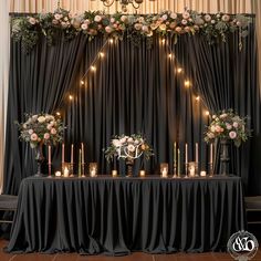 a table with candles and flowers on it in front of a black drape curtain