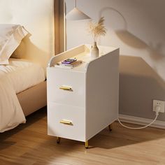 a white night stand next to a bed with a phone on it and a plant in the corner