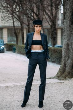 a woman standing in front of a tree wearing a black suit and hat with her hands on her hips