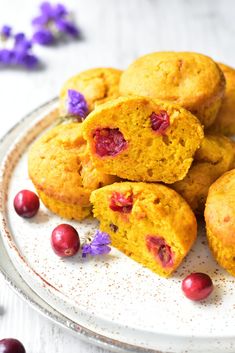 some muffins on a plate with cranberries and purple flowers around them