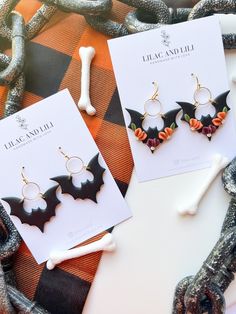 two bat shaped earrings sitting on top of a piece of paper next to a bone