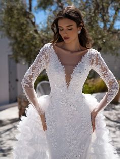 a woman wearing a white wedding dress with long sleeves and an open back, standing in front of a tree