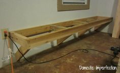 a wooden bench sitting on top of a floor next to a power cord and plugged in