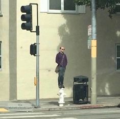 a man standing on the corner of a street next to a traffic light and trash can