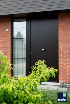 a black front door on a red brick building with green plants in the foreground