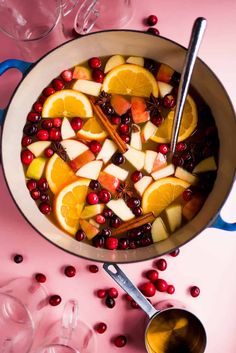 a pot filled with fruit and oranges on top of a pink tablecloth next to wine glasses