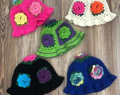 four crocheted hats with flowers on them sitting on a wooden floor next to each other