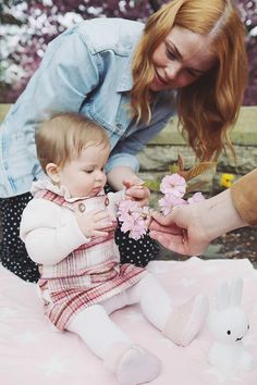 a woman is holding a baby with flowers in her hand while sitting on the ground