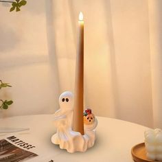 a lighted candle with two ghost figures on it sitting on a table next to a book