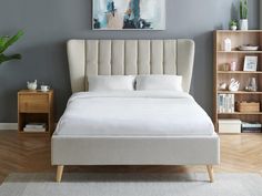 a white bed sitting in a bedroom on top of a hard wood floor next to a book shelf