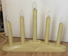 four candles are placed on a stand in the middle of a room with a white wall behind them