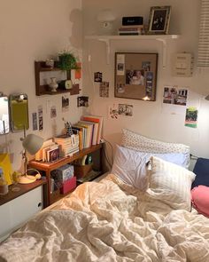 an unmade bed in a small room with pictures on the wall and shelves above it