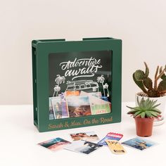 a green box with photos and magnets next to a potted plant on a white table