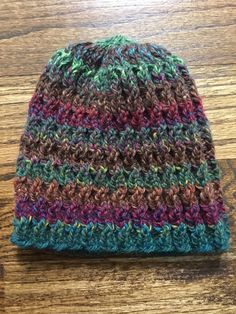 a multicolored crocheted hat sitting on top of a wooden table next to a pair of scissors