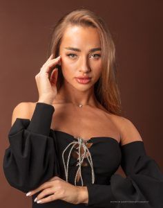 a beautiful young woman in a black dress holding her hand to her ear and looking at the camera