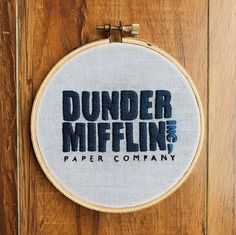 an embroidered hoop hanging on a wooden door that says dunder mifflin paper company