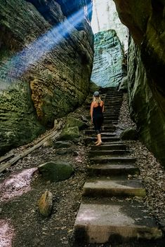 a woman is walking up some stairs in a cave with sunlight streaming through the rocks